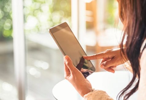 Close-up of woman with long brown hair holding an iPad and touching its screen